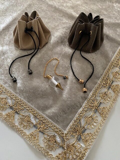 Pochons Rosa Plume pour pendule ou pierres de couleur beige posé sur une tapis de cartomancie